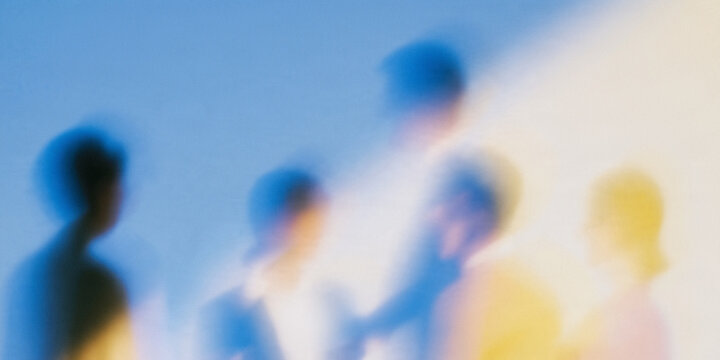 Abstract blurred silhouettes of business people against blue backdrop