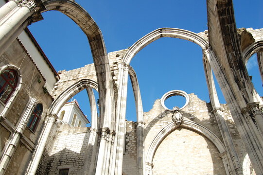 Low-angle view of the roofless Gothic arches and weathered stone walls of Carmo Convent in Lisbon, Portugal, dramatically framed against a deep blue sky.