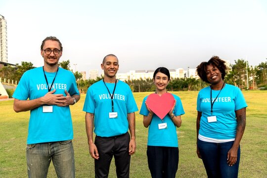 Group of diverse volunteers in blue shirts smiling outdoors.