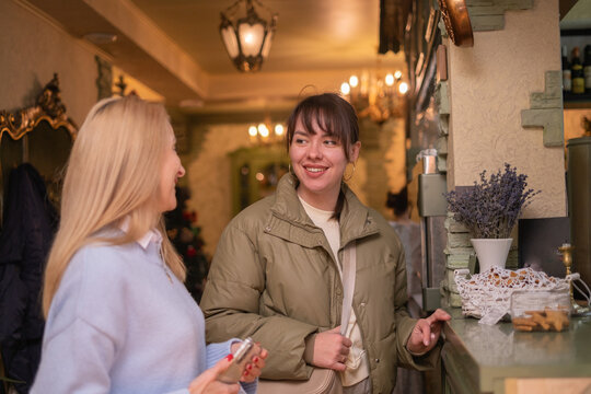 Two women chat inside a cafe during evening hours while enjoying warm drinks and pastries