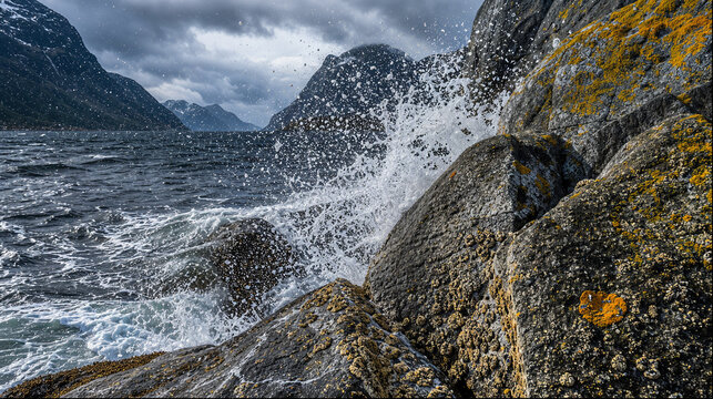 Waves crashing against lichen-covered rocks in a stormy fjord