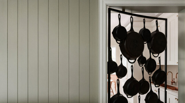 Hidden scullery featuring a pivoting French rail wall mounted with heavy black cast iron skillets in modern kitchen