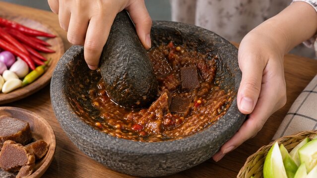 Hands making traditional spicy chili paste using a stone mortar and pestle