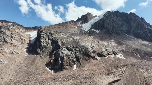 Cinematic drone flyover over rocky peaks, Oktyabrskaya cave, and shrinking ice blocks near Talgar Pass at 3400 meters altitude, revealing climate change and glacier melting in Tian Shan mountains near