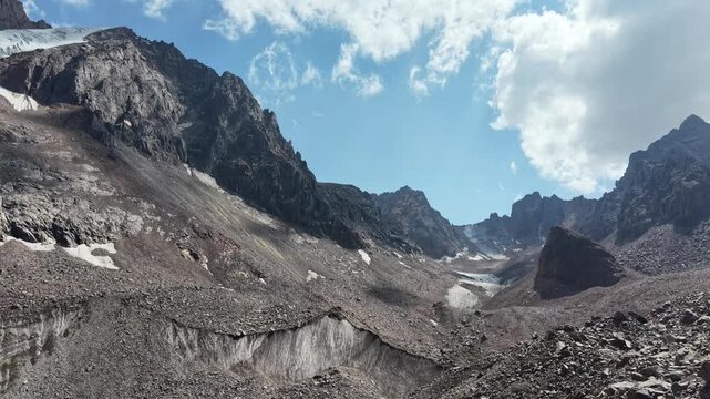 Cinematic drone flyover over rocky peaks, Oktyabrskaya cave, and shrinking ice blocks near Talgar Pass at 3400 meters altitude, revealing climate change and glacier melting in Tian Shan mountains near