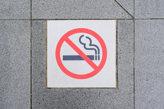 No smoking symbol displayed on a square pavement tile surrounded by gray stone paving, Tokyo, Japan