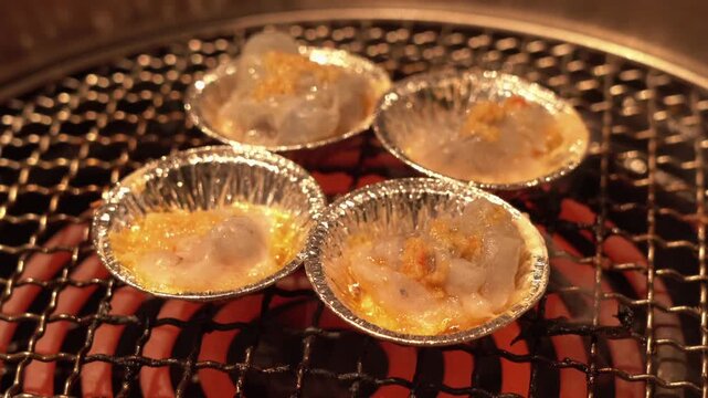 Grilled scallops with garlic butter in aluminum foil cups on glowing charcoal grill at Japanese yakiniku restaurant