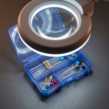 Magnifying lamp illuminating small electronic components and precision parts in a compartment organizer, close-up electronics repair and inspection concept