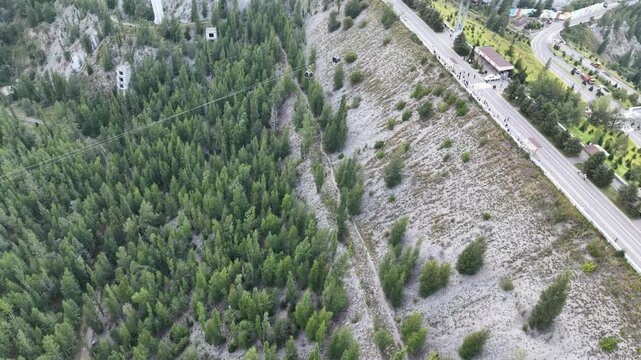Cinematic top-down drone flyover directly above crest of massive embankment mudflow control dam with steep slopes, protective forest, and access road in Almaty, Kazakhstan at summer sunset