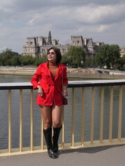 A woman wearing a red jacket and black boots stands on a bridge over the Seine river in Paris © iFocus