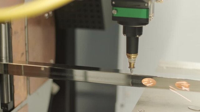 Automated CNC laser cutting machine processing a square metal pipe with bright sparks flying. Industrial metalworking, fabrication, and manufacturing process.
