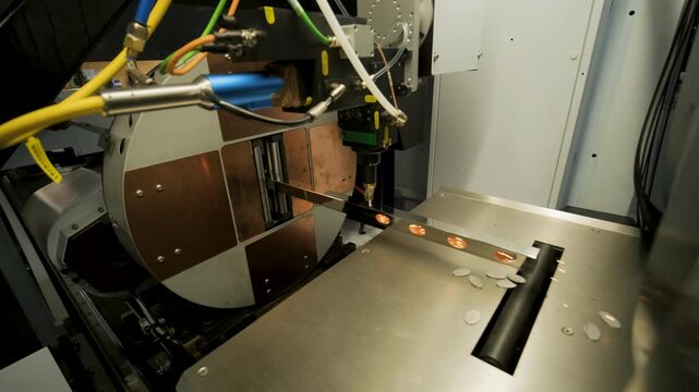Automated CNC laser cutting machine processing a square metal pipe with bright sparks flying. Industrial metalworking, fabrication, and manufacturing process.