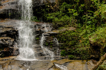 Tropical jungle waterfall in Thailand surrounded by lush green rainforest, moss-covered rocks, dense vegetation, and flowing water. The natural cascade creates a peaceful and refreshing scene © Yuliia