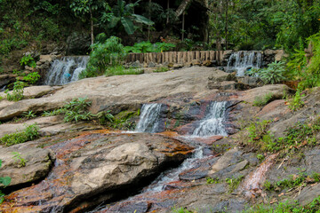 Tropical jungle waterfall in Thailand surrounded by lush green rainforest, moss-covered rocks, dense vegetation, and flowing water. The natural cascade creates a peaceful and refreshing scene © Yuliia