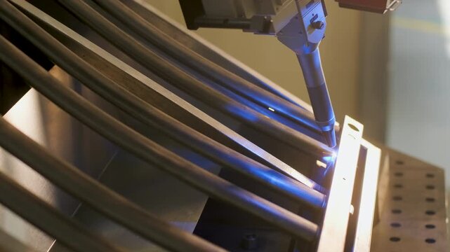 Automated CNC welding machine process, where a robotic nozzle joins metal tubes with a bright blue glow from the welding arc. Industrial metalworking, automation, and high-precision fabrication of ste