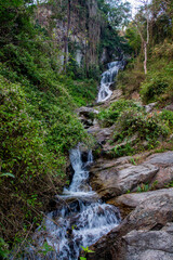 Tropical jungle waterfall in Thailand surrounded by lush green rainforest, moss-covered rocks, dense vegetation, and flowing water. The natural cascade creates a peaceful and refreshing scene © Yuliia