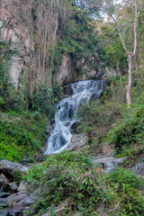 Tropical jungle waterfall in Thailand surrounded by lush green rainforest, moss-covered rocks, dense vegetation, and flowing water. The natural cascade creates a peaceful and refreshing scene © Yuliia