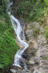 Tropical jungle waterfall in Thailand surrounded by lush green rainforest, moss-covered rocks, dense vegetation, and flowing water. The natural cascade creates a peaceful and refreshing scene © Yuliia
