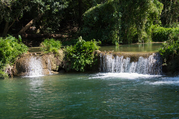 Tropical jungle waterfall in Thailand surrounded by lush green rainforest, moss-covered rocks, dense vegetation, and flowing water. The natural cascade creates a peaceful and refreshing scene © Yuliia