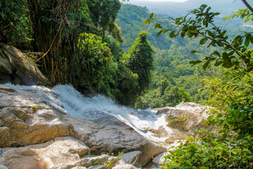 Tropical jungle waterfall in Thailand surrounded by lush green rainforest, moss-covered rocks, dense vegetation, and flowing water. The natural cascade creates a peaceful and refreshing scene © Yuliia