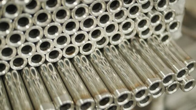 Close-up of a large stack of shiny, polished stainless steel metal tubes arranged in a uniform pattern. Industrial background showing clean cylindrical pipes ready for manufacturing or construction.