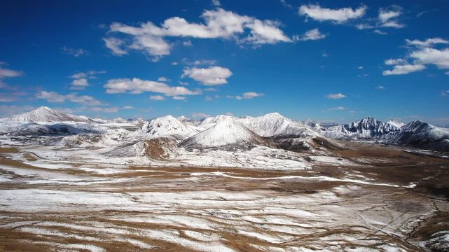 Open Tibetan mountain basin patterned with snow and brown earth