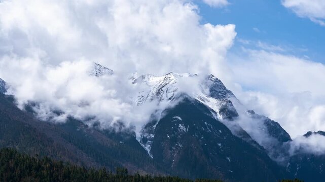 Snowy Tibetan mountain range above forests and rolling clouds