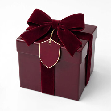 A luxury dark red square gift box with velvet ribbon and blank shield tag isolated on white background