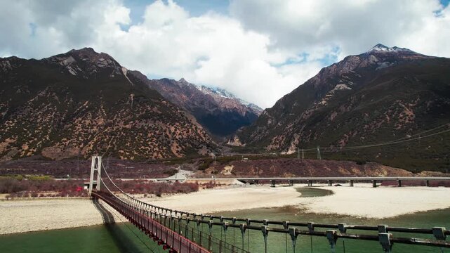 Bridges over pale river sediment below rugged Tibetan mountains