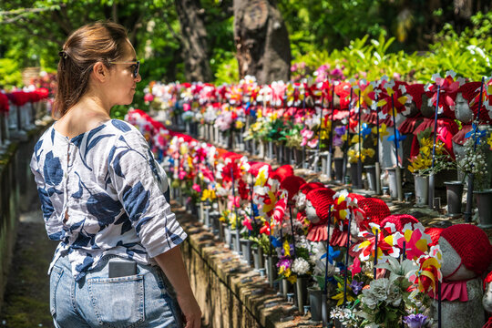 Turista mirando simp&aacute;ticas estatuas jizo vestidas con sombreros y tapados en un Santuario Japones, en Kioto.	