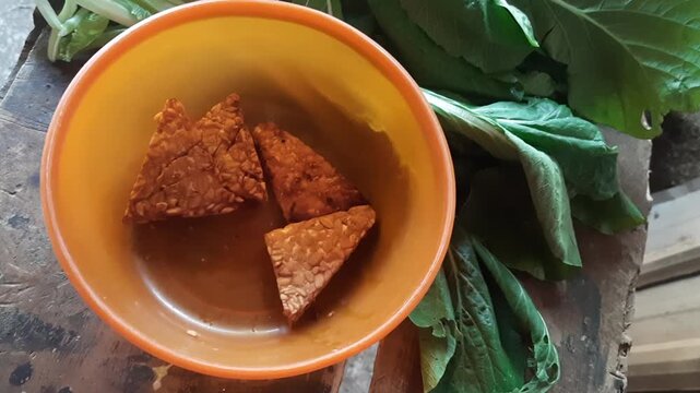 Hand Picking Fried Tempeh from Orange Bowl - Indonesian Traditional Food`
