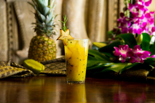 Refreshing tropical fruit cocktail garnished with starfruit and rosemary on a wooden table