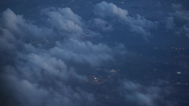 Aerial view of city lights at night through fluffy clouds from airplane window
