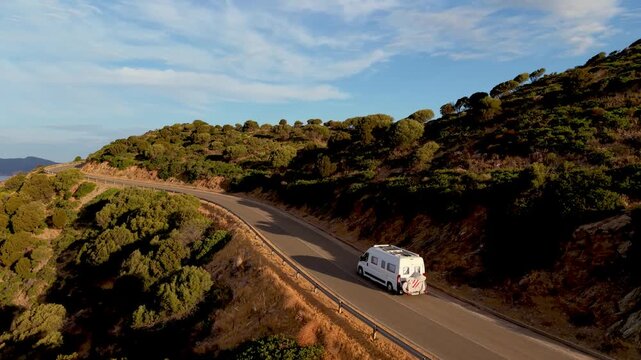 Experience the breathtaking beauty of Sardinia, Italy as a camper van navigates through winding coastal roads surrounded by lush hills and serene landscapes.