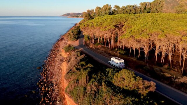 Witness the stunning beauty of Cagliari, Sardinia, as the sun sets over the serene coastline. a camper van or rv motorhome riding the coastal road