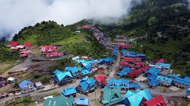 Elevated aerial view of a remote high-altitude mountain village with brightly colored blue and red tin roofs enveloped in rolling clouds.