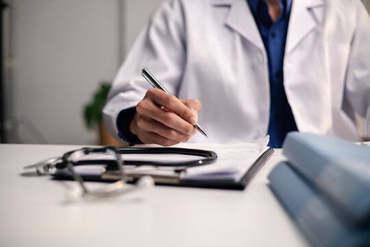 A doctor reviews a medical form beside a stethoscope and blue folders. The image represents clinical documentation, health insurance claims, medical billing and healthcare administration.