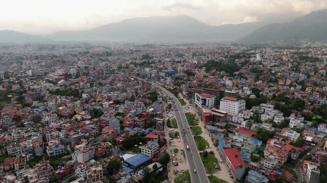 Aerial perspective of a multi-lane divided highway with green medians traversing a vast, densely packed city towards distant mountains.