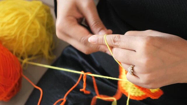 Close up footage of woman hands crocheting colorful yellow and orange woolen fabric at home