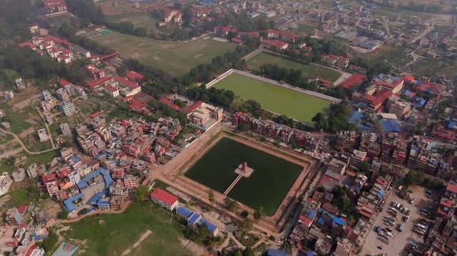 Cinematic drone view of a beautiful temple and lake next to a large green stadium surrounded by Kathmandu's dense city center