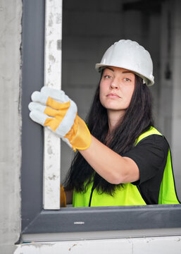 Young female construction worker with protective gloves and helmet checking building window using spirit level