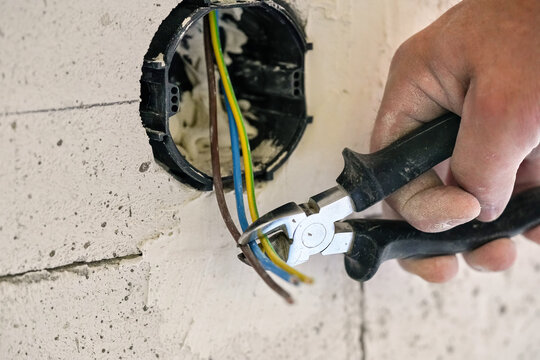 Electrician construction worker, adjusting electric cabling with wire cutters installed in black plastic box on a wall, closeup detail