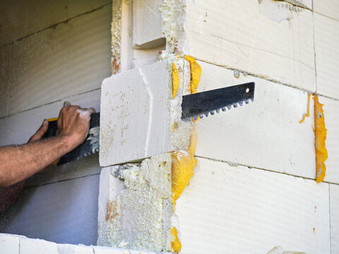 Construction builder worker cutting piece of foam insultation and brick at frame wall to make it straight, closeup detail
