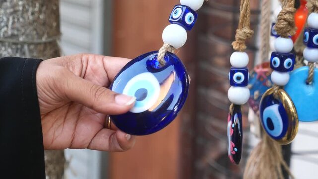 Woman's hand holding a blue evil eye charm, protection symbol with beads