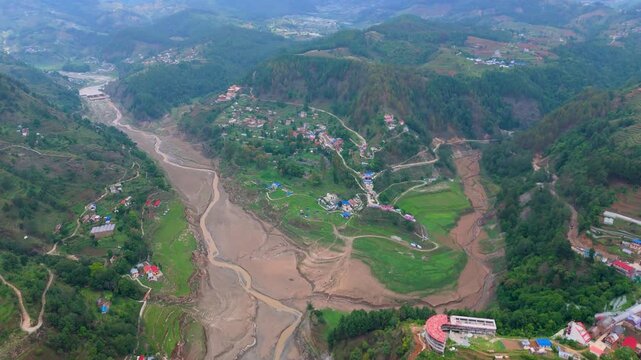 Wide aerial landscape showing extensive flood sediment and mud inundation across a mountain river basin bordered by terraced fields in Nepal