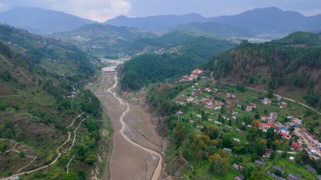 Aerial drone view of a river valley inundated with heavy sediment and muddy flood deposits beside a rural hillside village in Nepal