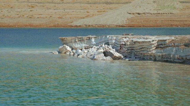 Dead Sea shore on Jordan side, layers of sand and salt visible at coast, calm blue water near