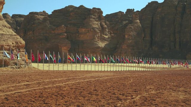 Row of different world countries flags waving in slow wind near large rocky cliff