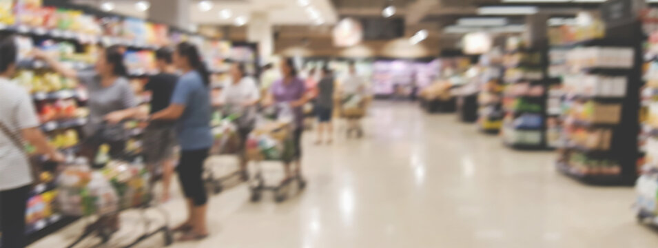 Abstract blurred grocery store scene with shoppers and a cart near the produce section, suitable for supermarket advertising with copy space.