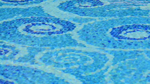 Gentle ripples of clear, sunlit water create shimmering caustics over an intricate blue mosaic tile pattern on a swimming pool floor.